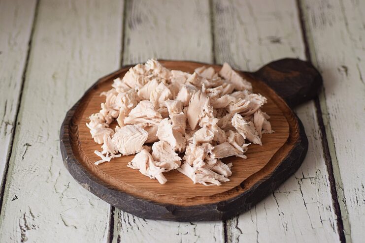Dicing the Cooked Chicken - Chop the boiled chicken fillet into small, bite-sized pieces. Cooked chicken fillet being chopped into small pieces on a cutting board.