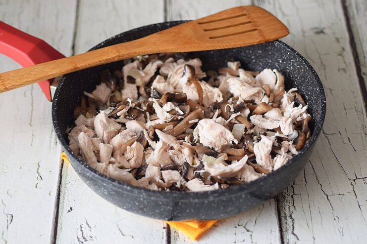 Combining Ingredients - Add the chicken to the mushrooms, reduce the heat, and mix well. Diced chicken being added to the frying pan with mushrooms, onion, and garlic.