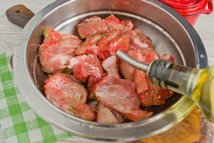 Adding oil helps the spices adhere and creates a crispy crust. Seasoned pork slices in a bowl being drizzled with oil.