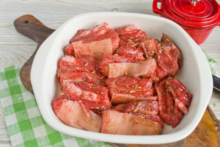 Arrange the seasoned pork in a single layer for even cooking. Seasoned pork slices arranged in a glass baking dish, ready for the oven.