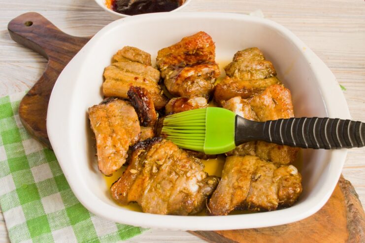 Brushing with a honey-soy glaze adds flavor and creates a beautiful crust. Pork slices in a baking dish being brushed with a dark glaze.