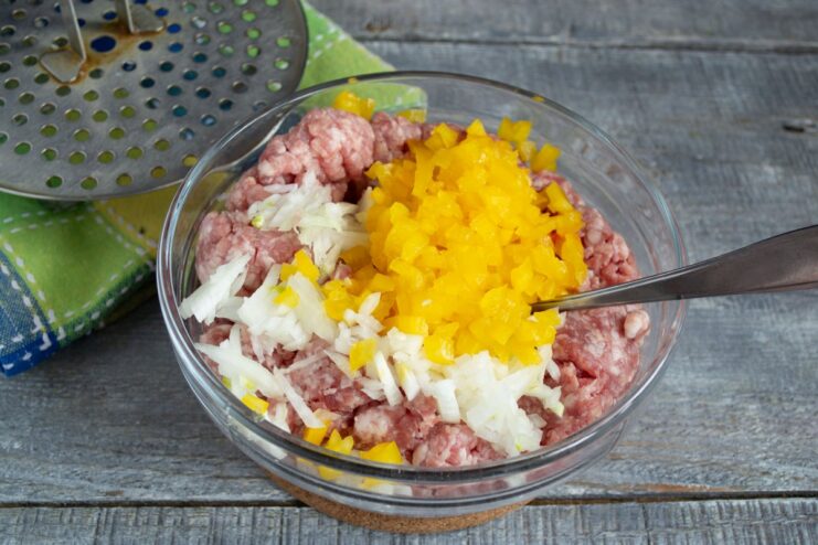 Incorporating Diced Bell Pepper into the Meat Mixture Diced red bell pepper being added to the minced meat and onion mixture.