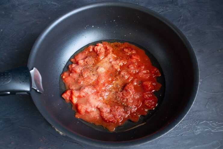 Starting the rich and flavorful Koshari tomato sauce Canned tomatoes and spices being added to a wok with olive oil.