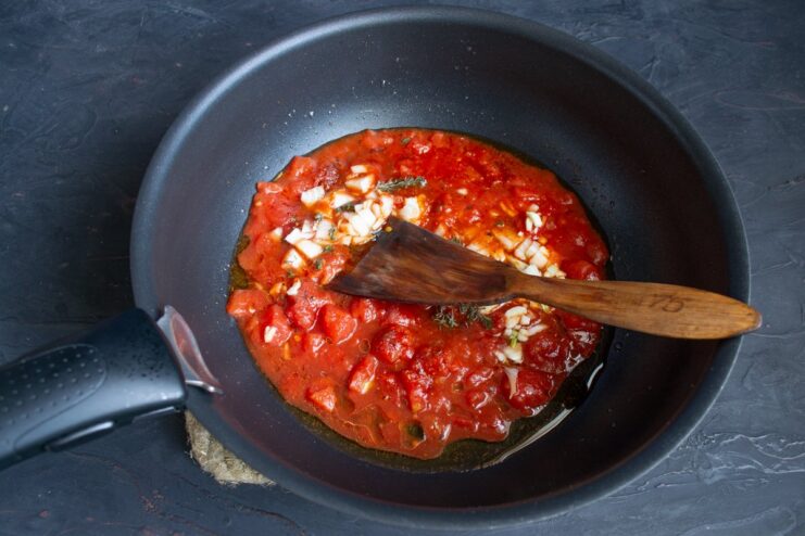 Building the aromatic base for the tomato sauce Chopped onion, garlic, and thyme being cooked in a tomato sauce in a wok.