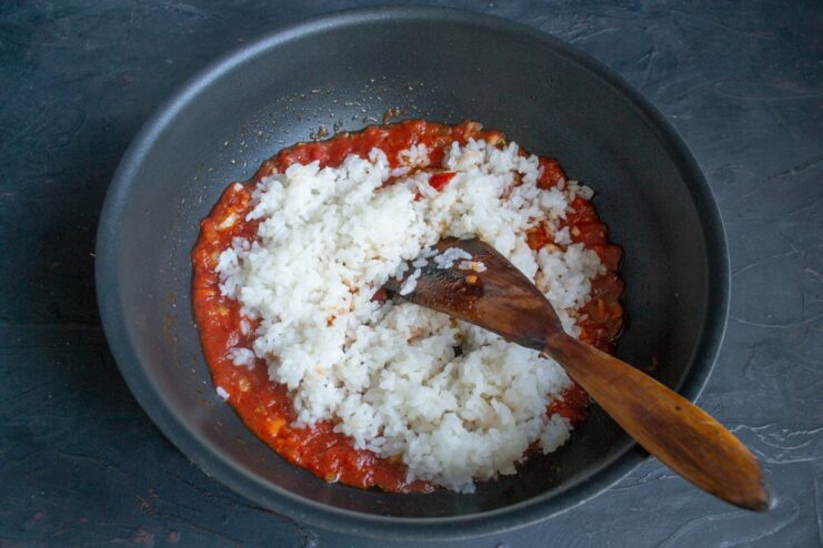 Combining the cooked rice with the savory tomato sauce Cooked white rice being added to the tomato sauce in a wok.