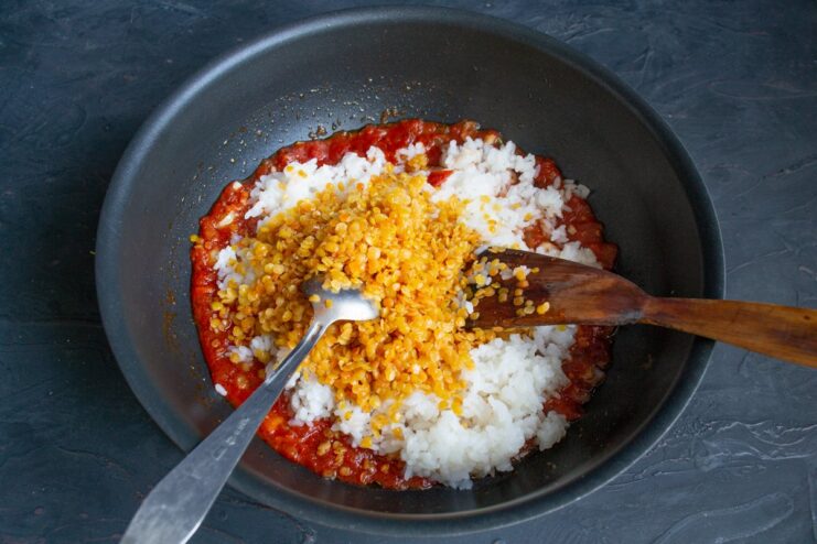Adding protein-rich lentils to the Koshari mix Cooked lentils being added to the rice and tomato sauce mixture in a wok.
