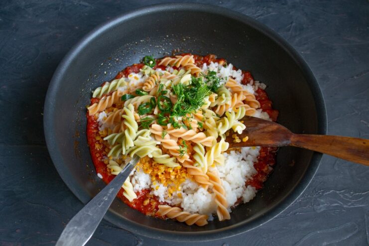 The final ingredients for a perfect Koshari Cooked pasta, fresh herbs, and sliced chili added to the Koshari in the wok.