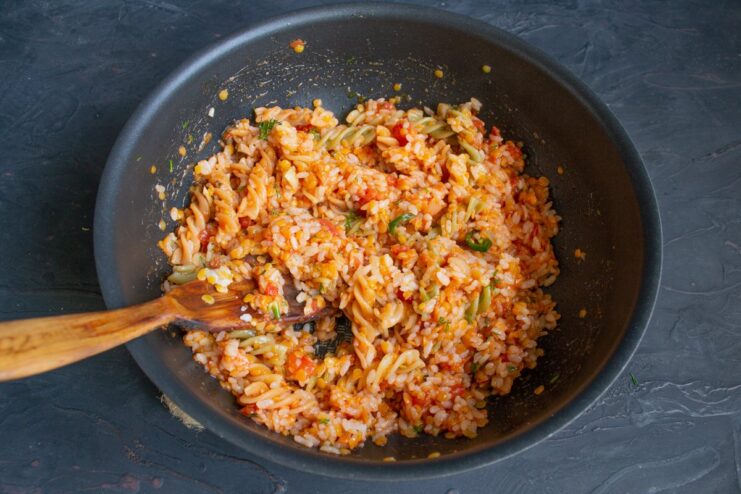 Gently mixing all Koshari components together All Koshari ingredients—rice, lentils, pasta, and sauce—being mixed in a wok.