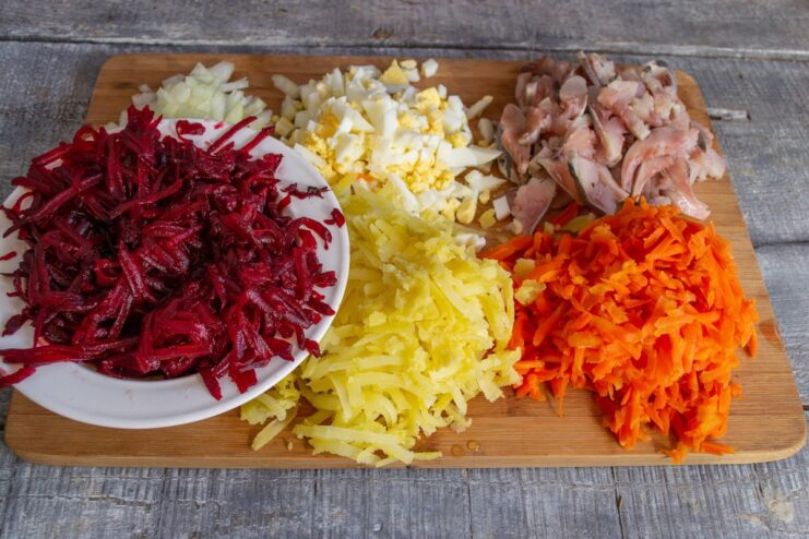 All Ingredients for Herring Under a Fur Coat Salad, Prepped and Ready Bowls of prepped ingredients for Selyodka pod Shuboy: grated beets, carrots, potatoes, diced herring, onions, and eggs.