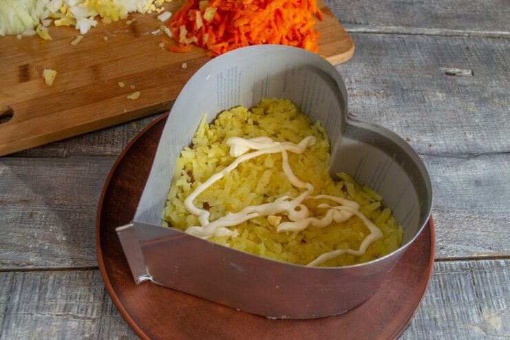 Step 2: Adding the Potato and Mayonnaise Layer Grated potatoes layered over herring in a food ring, being spread with a layer of mayonnaise.