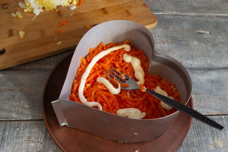 Step 4: Adding Grated Carrots and a Mayo Drizzle A layer of grated carrots in the food ring, topped with a lattice pattern of mayonnaise.