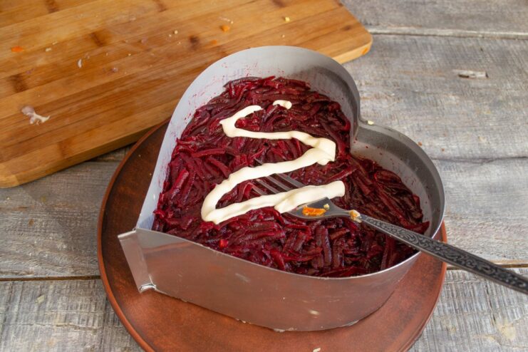 Step 6: Adding the Final Layer of Grated Beets Grated boiled beets being added as the top layer of the Selyodka pod Shuboy salad.