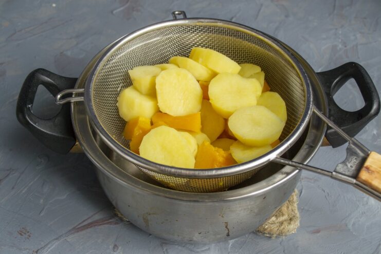 Step 4: Draining the cooked vegetables thoroughly Boiled potatoes and pumpkin being drained in a metal sieve over a sink.
