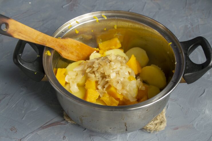 Step 5: Combining cooked vegetables with sautéed onions Drained potatoes and pumpkin in a pot with sautéed onions on top.