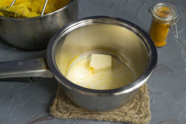 Step 7: Preparing the spiced cream mixture A saucepan with cream, butter, and turmeric being heated on a stove.