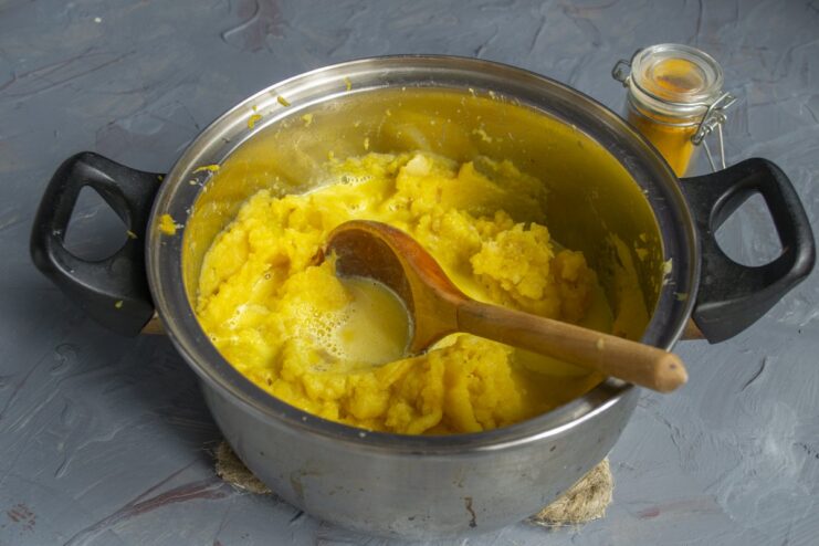Step 8: Adding the hot cream to the mashed vegetables Pouring the hot, yellow cream mixture into the pot of mashed potatoes and pumpkin.