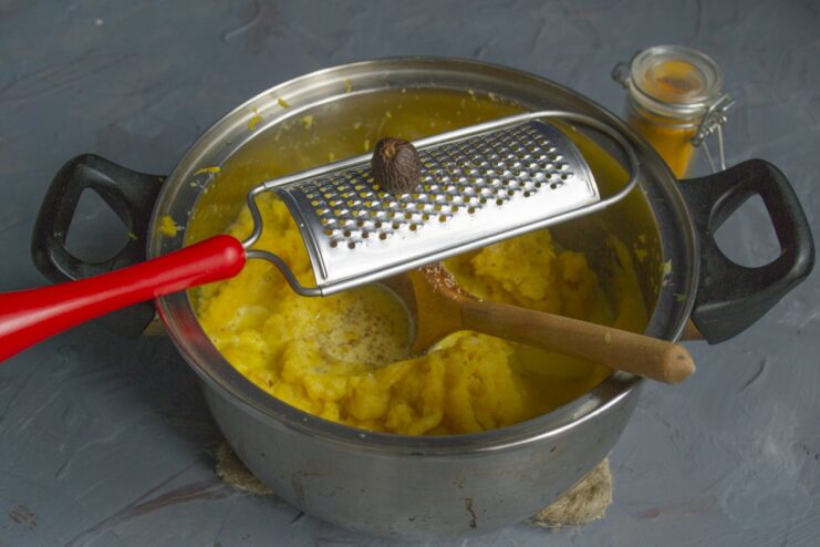 Step 9: Seasoning with fresh nutmeg and mixing Grating fresh nutmeg into the mashed potato and pumpkin mixture in a pot.