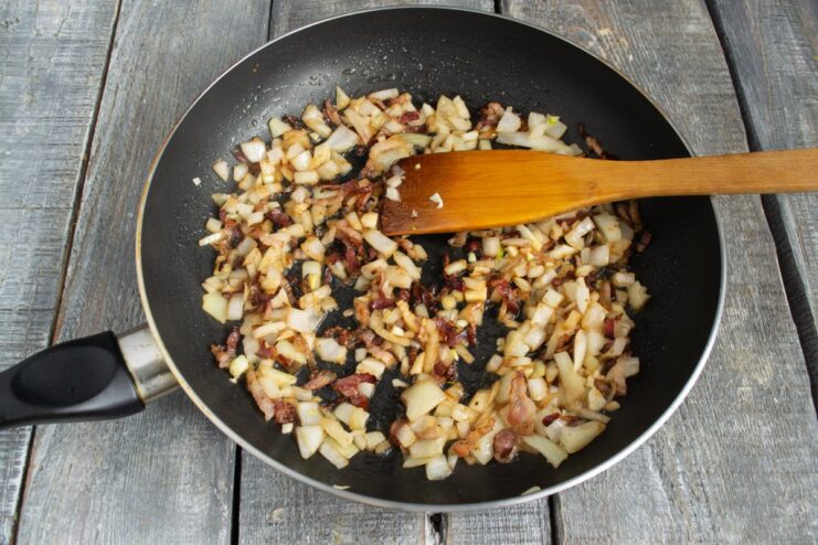 Sautéing Onions and Garlic with Bacon for an Aromatic Stew Chopped onions and garlic being sautéed with fried bacon in a pan.