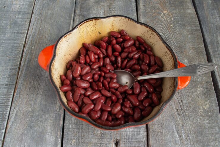 Layering the Stew: Starting with Cooked Beans Cooked red beans being placed at the bottom of a Dutch oven.