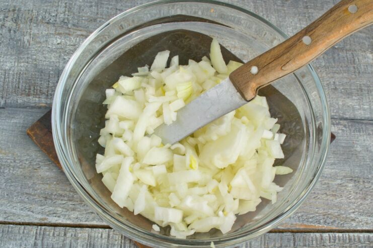 Finely Chopping Onion for the Soup Base A hand holding a knife, finely chopping a yellow onion on a wooden board.