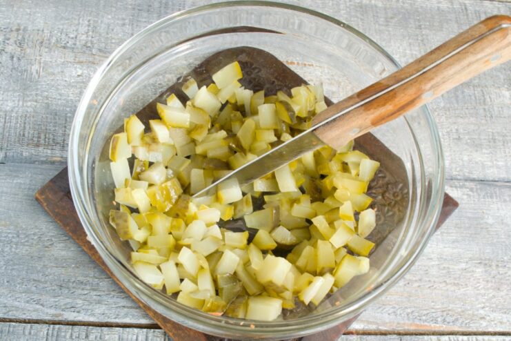 Dicing Pickles - The Key Ingredient for Rassolnik Dill pickles being diced into small cubes on a white cutting board.