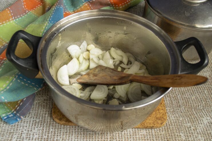 Sautéing onions and garlic in a heavy-bottomed pot to build the flavor base. Sliced onions and garlic being sautéed in oil in a pot.