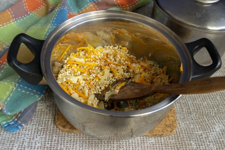 Toasting the pearl barley with vegetables to enhance its nutty flavor. Pearl barley being toasted with vegetables in a pot.