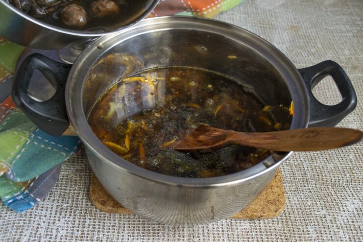 Combining the toasted barley with hot mushroom broth and cooked mushrooms. Hot mushroom broth and cooked mushrooms being added to the barley and vegetables.