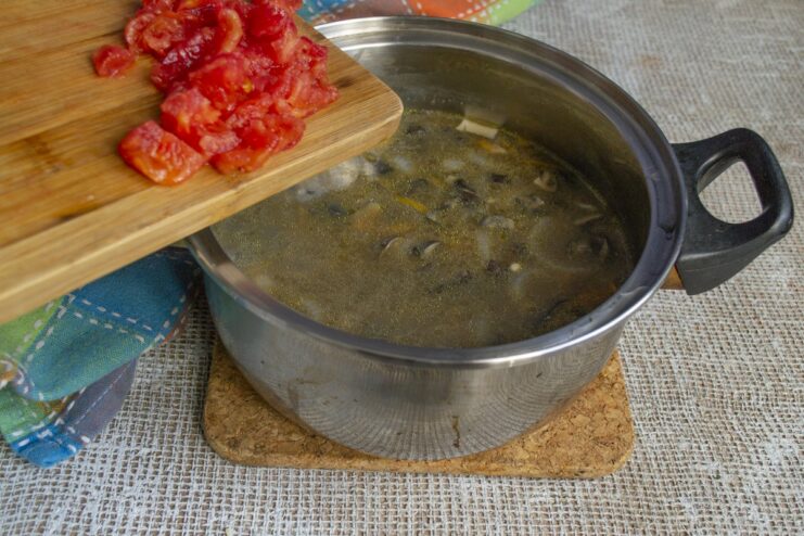Adding fresh diced tomato for a touch of sweetness and acidity. Diced tomatoes being added to the pot with barley and mushrooms.