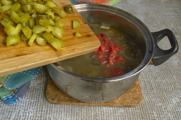 Adding tangy fermented pickles and seasoning the dish. Diced fermented pickles being added to the pot and stirred in.
