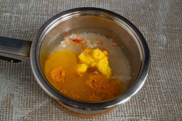 Flavoring the Rice: Adding Turmeric and Saffron for Color and Aroma Spices like turmeric and saffron being added to the rice and water in a pot.