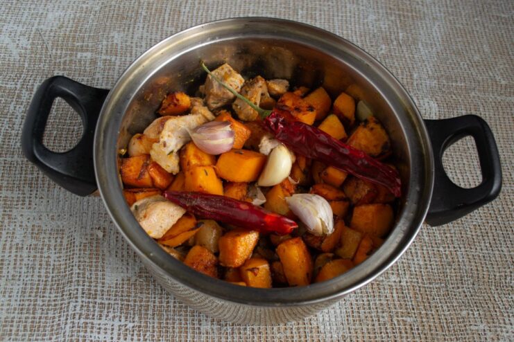 Adding Aromatics: Chili and Garlic for Extra Flavor Dried chili peppers and crushed garlic cloves placed on top of the pumpkin layer.
