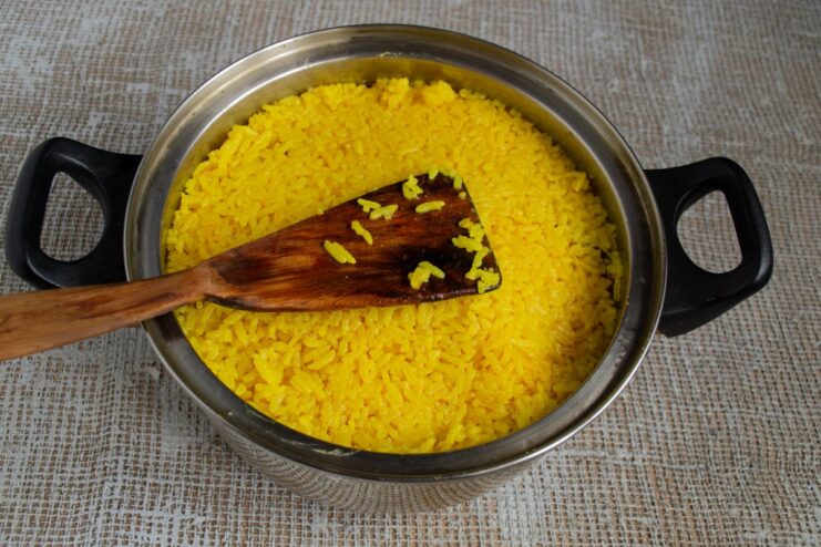 The Final Layer: Covering Everything with Fragrant Saffron Rice A thick layer of cooked rice covering meat and vegetables, with holes for the broth.