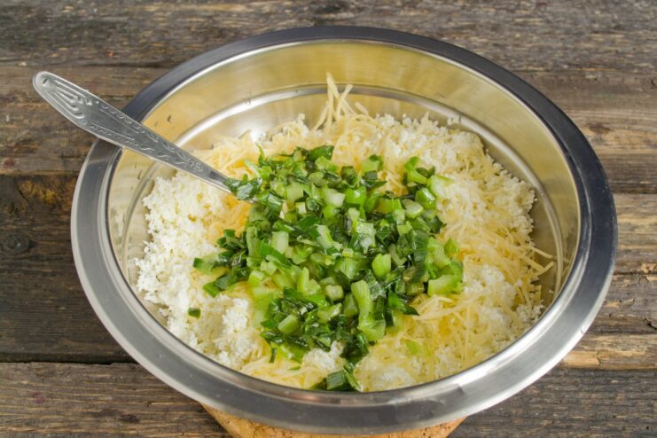 Building the Savory Base: Sautéed Onions Join the Cheese Filling Sautéed green onions being added to the cheese and tvorog mixture in a bowl.