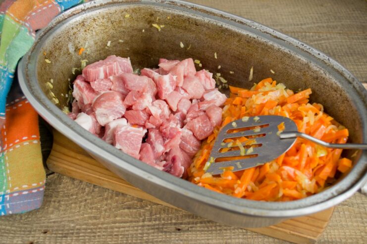 Browning the pork to lock in juices and add rich flavor. Cubes of pork being browned in the Dutch oven next to the sautéed vegetables.