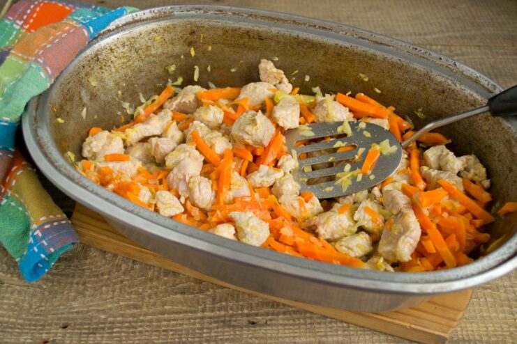 Combining the browned pork and vegetables to meld the flavors. Pork, onions, and carrots mixed together and cooking in the Dutch oven.