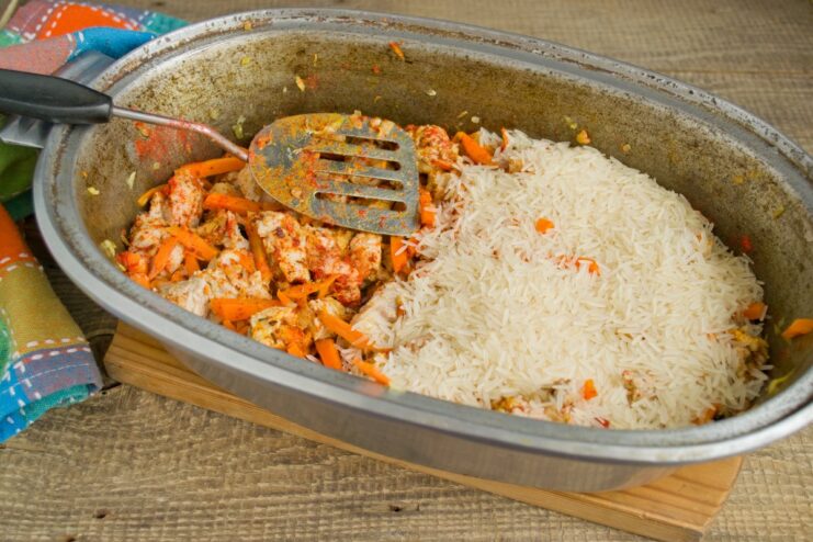 Layering the rice evenly over the meat without mixing. An even layer of uncooked basmati rice covering the meat and vegetables in the pot.
