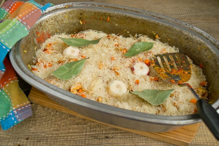 Adding whole garlic heads and bay leaves for deep, aromatic flavor. Halved garlic heads and bay leaves being placed on top of the rice layer.