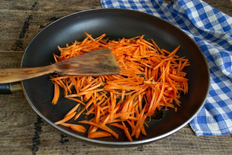Thinly sliced carrots being added to a hot frying pan with oil.