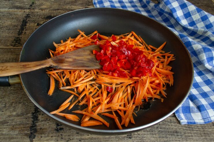 Diced red bell pepper being added to the frying pan with carrots.