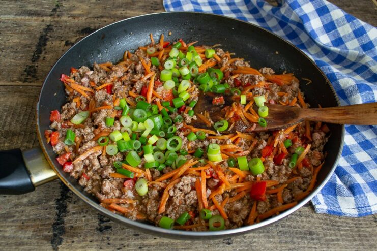 The ground beef and vegetable mixture being cooked and seasoned in the pan.