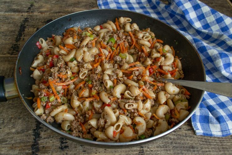 The final dish of spelt pasta and beef sauce being mixed and heated in a pan.