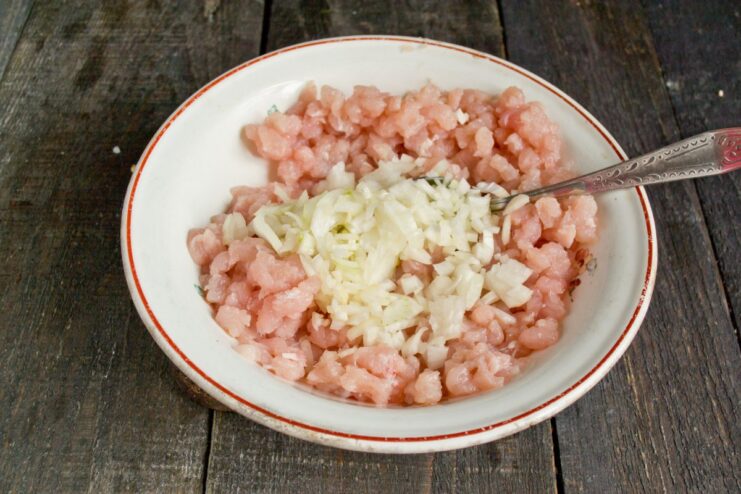 Adding Finely Chopped Onion to the Chicken Mince A bowl of minced chicken with finely chopped onions being added on top.