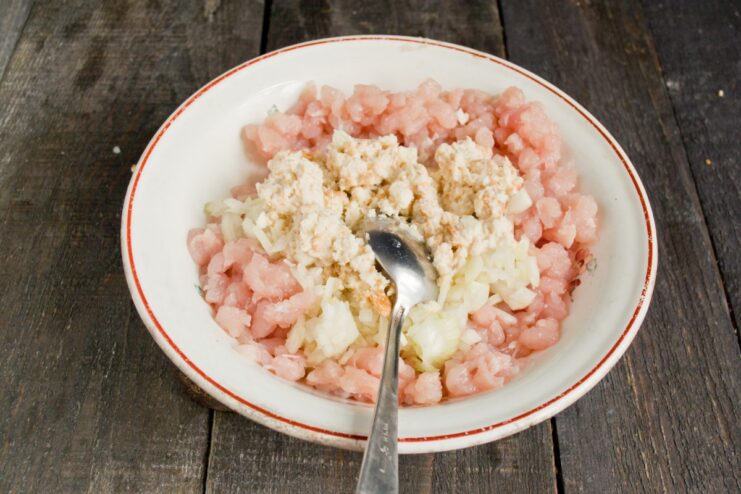 Mixing Soaked Bread into the Cutlet Mixture Soaked white bread paste being added to a bowl with minced chicken and onions.