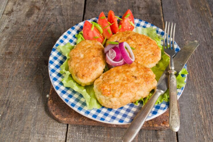 Serving Juicy Chicken Cutlets with a Fresh Side Salad A serving of golden minced chicken cutlets on a plate with a fresh vegetable salad.