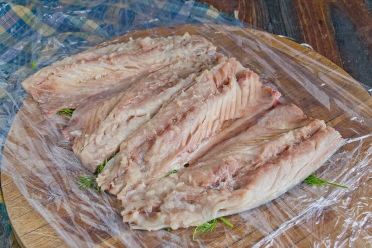 Arranging Mackerel Fillets to Form a Rectangle Two mackerel fillets arranged skin-side down on cling film to form a rectangular base.