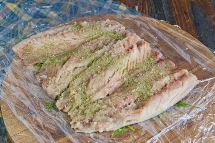 Seasoning the Mackerel Fillets Before Adding the Filling Mackerel fillets being sprinkled with salt, spices, and dry gelatin powder.