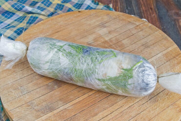 Tightly Rolling the Mackerel Roulade in Cling Film The mackerel roulade being rolled tightly in multiple layers of cling film.