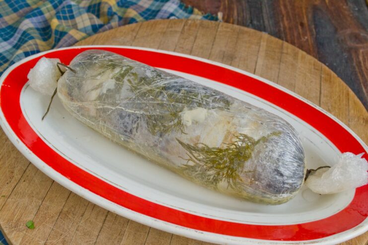 The Cooked Roulade Chilling to Set Firmly The cooked mackerel roulade, still wrapped in cling film, resting on a plate before chilling.
