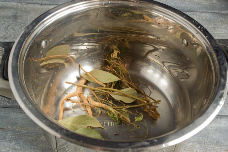 Step 1: Adding Aromatic Spices to the Pot for the Pork Knuckle Broth A close-up of various spices like bay leaves and parsley root at the bottom of a large pot.